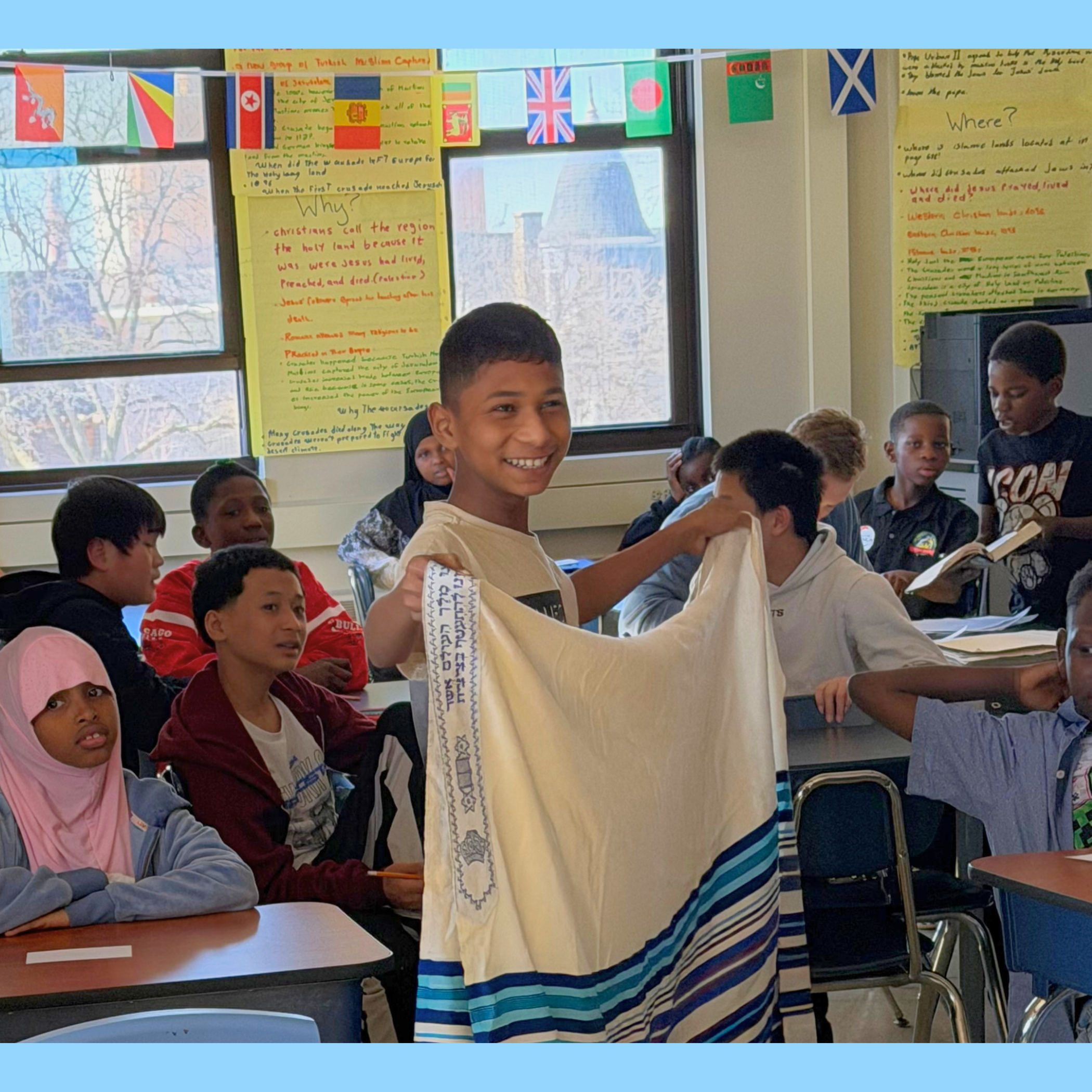 Student smiles as they hold and ask questions about a tallit. Jewish prayer shawl in a Student to Student workshop. The student is surrounded by a classmates from different religious and cultural backgrounds.