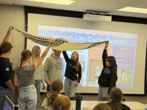 Spreading Jewish joy: High school students briefly enact what to expect at a Jewish wedding as they improvise a chuppah using a tallis (Jewish prayer shawl) during a peer led presentation from Student to Student presenters.